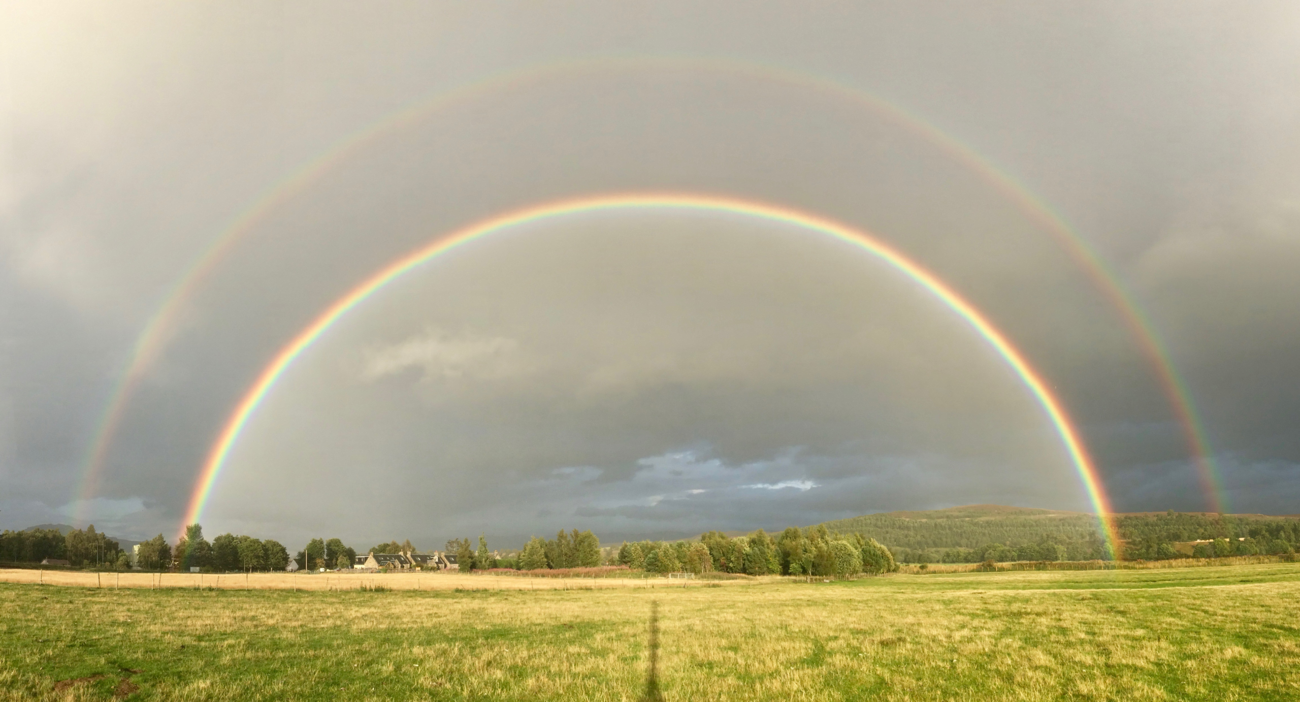 An intense double rainbow over grassy fields.
