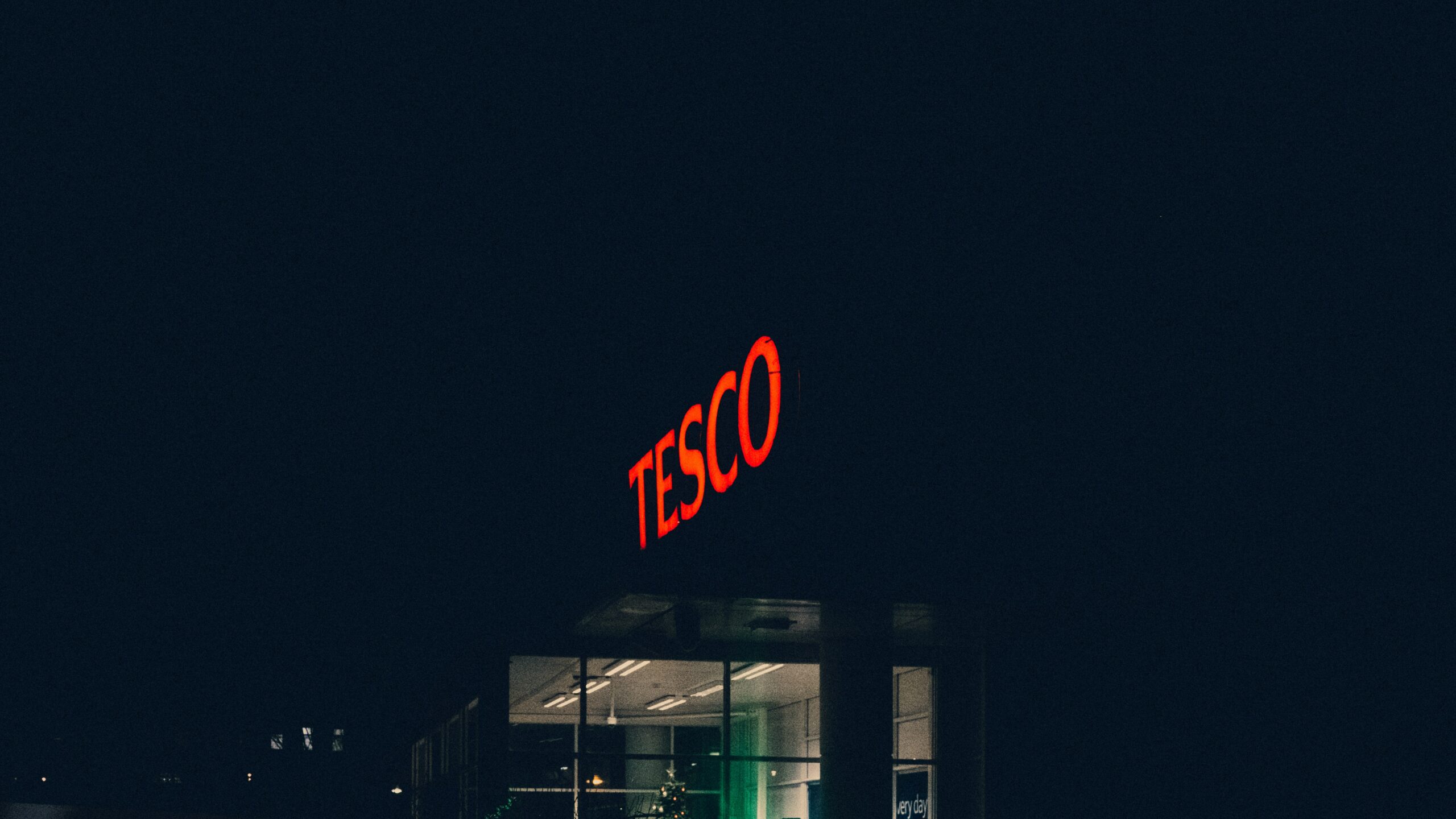 Red illuminated "Tesco" sign in the dark.